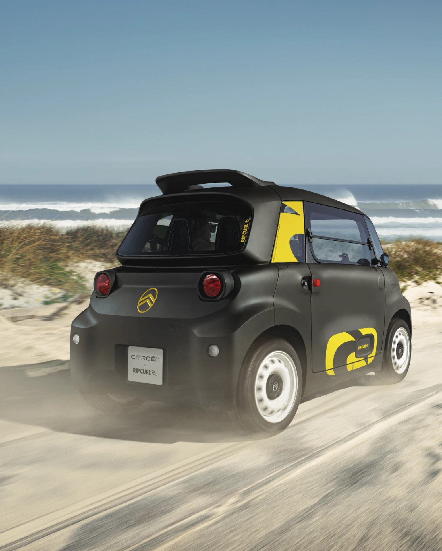 Vista posteriore tre quarti in guida Citroën Ami x Rip Curl elettrica senza patente, Citroën Ami guida divertente per auto elettrica urbana