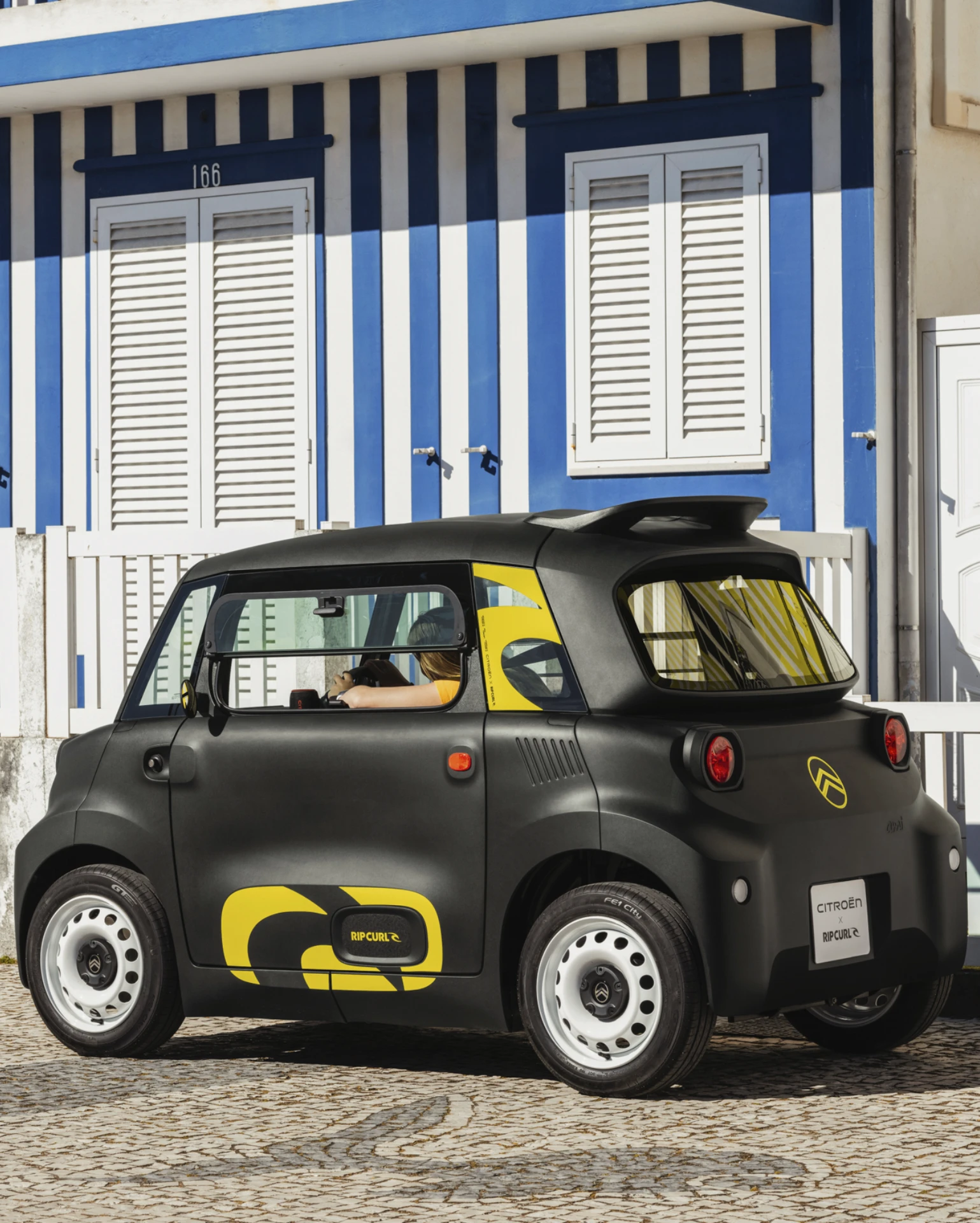 Vista posteriore laterale in strada Citroën Ami x Rip Curl elettrica senza patente, Citroën Ami quattro ruote più sicure per auto elettrica urbana
